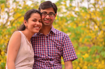 Young Indian couple smiling standing against yellow golden shower amaltas leaves during summer autumn weather in Delhi, India