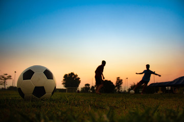 Silhouette action sport outdoors of a group of kids having fun playing soccer football for exercise in community rural area under the twilight sunset sky.