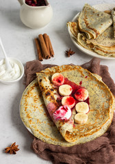 Vanilla poppy seed pancakes or crepes with natural yogurt, banana and cherry sauce with spices (cinnamon and anise). Light concrete background. Copy space.