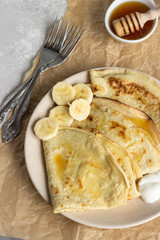 Thin pancakes or crepes with natural yogurt, honey and banana on a plate. Light concrete background. Copy space.