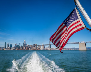 American flag waving in front of San Francisco skyline and the Bay Bridge