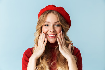 Portrait of optimistic blond woman 20s wearing red beret smiling while standing, isolated over blue...