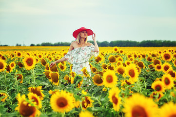 A young woman in a wide-brimmed hat walks in a field with sunflowers