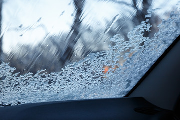 Snow-covered car windshield with melted snow drops. Blurred background. Copy space. Winter concept