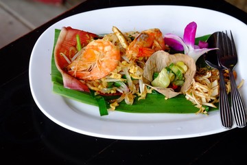 Fried noodle of Padthai with shrimps on top, a Thai famous food in a white plate on black dinning table 