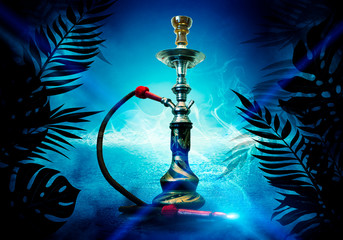 Obraz premium Hookah on the background of tropical leaves and a brick wall. Neon light, laser figures in smoke