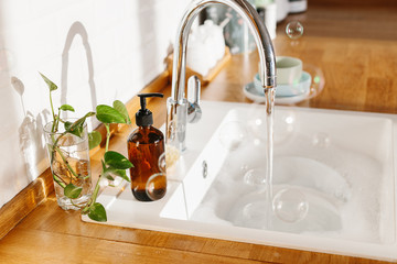 White sink glass soap dispenser bamboo dish washing brush wooden countertop and white ceramic brick...