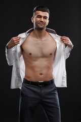 Charismatic sexy man takes off white shirt isolated on black background.