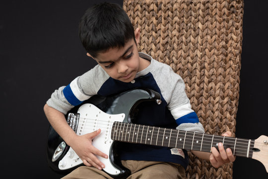 8 year old British Indian boy practices the electric guitar at home. 