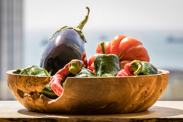 Wooden bowl with a natural hole in the side filled with chilies a tomato and an eggplant on a...