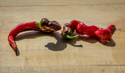 Two curling cayenne peppers on a wooden block next to each other with a short shadow