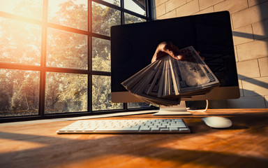 Hand giving money from computer screen. The concept of income from technology and internet work...