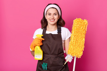 Cheerful young housewife wears white t shirt, brown apron with green clothespins, orange rubber...
