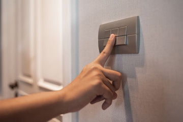 Asian female right hand is turning off on grey light switch.