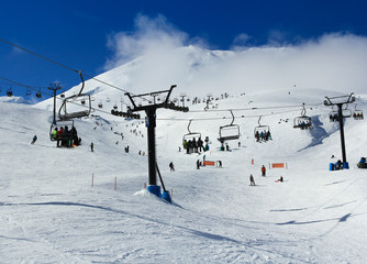 skiers, snowboarders and tourist traveling in cable cars in a snow covered misty mountain with a clear blue sky. 