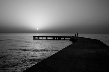 Fisherman at sunrise catch prey at dawn on the old pier in the sea, black and white photo.