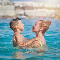 Attractive European woman hand her son swimming in the ocean during their vacations.