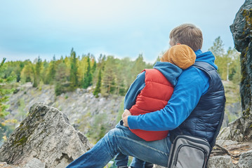 Active European man and his son are sitting on the big stone near the picturesque canyon. They are enjoying fresh air and serenity around.