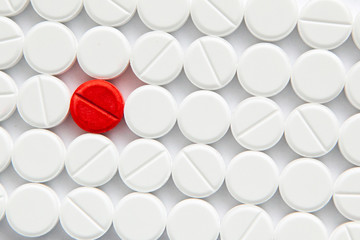 Top view of a pile of white medicine pills on a white surface. One tablet of red medication. Vaccine concept 