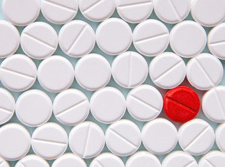 Top view of a pile of white medicine pills on a white surface. One tablet of red medication. Vaccine concept 