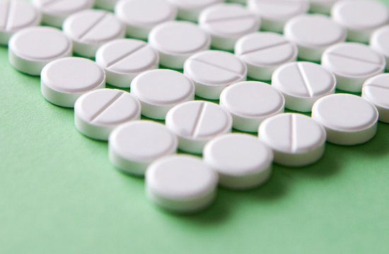 Top view of a pile of white medicine pills on a white surface. One tablet of red medication. Vaccine concept 