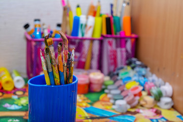 Photo of old brushes for painting, stand in a jar. Children's drawing area, old brushes, on the background of paint and pencils.