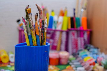 Photo of old brushes for painting, stand in a jar. Children's drawing area, old brushes, on the background of paint and pencils.