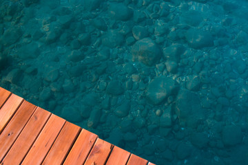 Part of the wooden pier and clear water sea water, visible stones