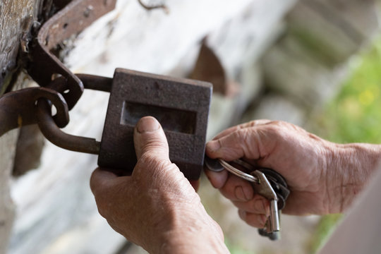 Old man hands holding metal vintage lock and key to open close old wooden door