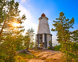 Ancient lighthouse on the shore among the pines at sunset.