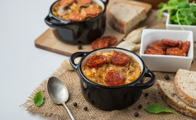Slovak Christmas national cabbage soup in two small black pots with sausage on the jute background.