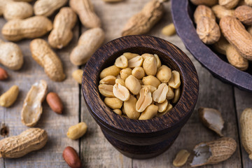 Peanuts in small dark wooden bowl on natural rustic desk.