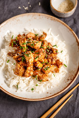 Top view on sesame chicken pieces with rice on a ceramic plate. Chinese traditional dish.