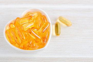 Fish oil capsules on a white wooden background, vitamin D supplement, selective focus.