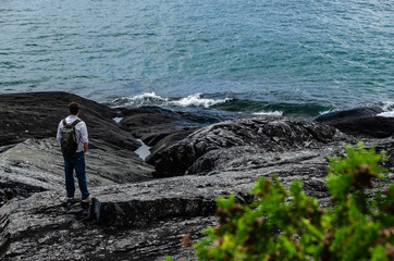 Fototapeta premium man standing on black rocky shore