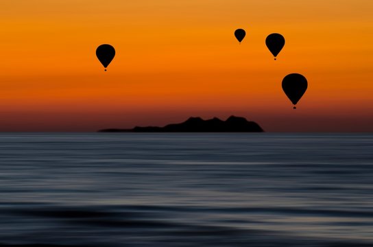 Bellissimo scenario con sagome di mongolfiere in volo sul mare al tramonto