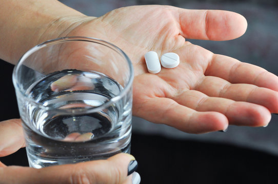 Hands with tablets and glass of water.