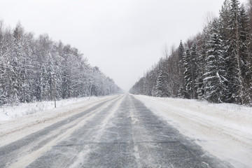 Fototapeta na wymiar winter road with ice on the asphalt, trees under snow during the winter frost in Russia