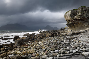 Tourists on rocks of Elgol beach at Port na Cullaidh with Red Cuillin Mountains under clouds on Loch Scavaig Isle of Skye Scotland UK