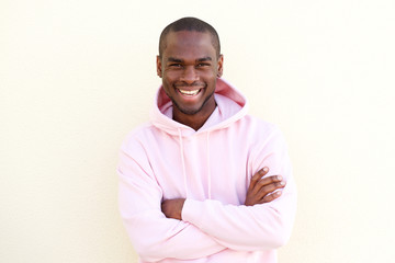 cool young black man smiling with arms crossed by light wall