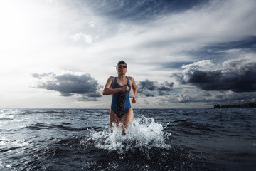 Young woman in swimsuit running in the water during triathlon competition