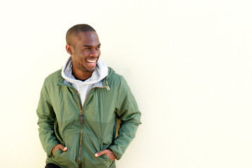 portrait of happy young black man in jacket smiling by wall