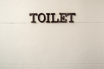Toilet word made from rustic metal hanging on white wall