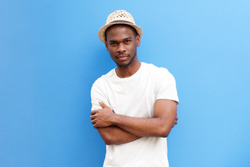cool young black guy with hat posing with arms crossed against blue background