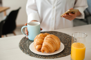 Woman in white shirt drinking coffee with croissants
