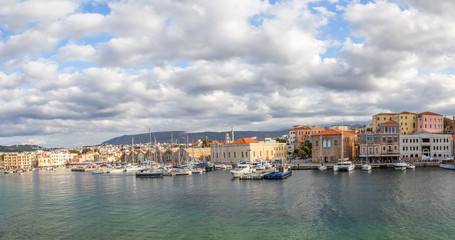 Fototapeta premium A panorama of the seaport town Chania, the island of Crete, Greece. A harbor with wooden pantons, moored yachts, ships, boats. Colorful architecture of modern and old houses. Mountains on the horizon.