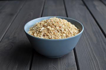 Rolled oats in ceramic bowl on dark wooden table background