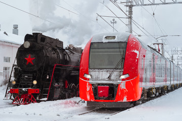 steam locomotive and modern multiple-unit train stand nearby at station