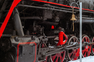 closeup of a steam locomotive wheels with station bell