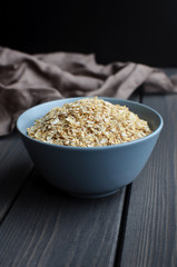 Rolled oats in ceramic bowl on dark wooden table with texture